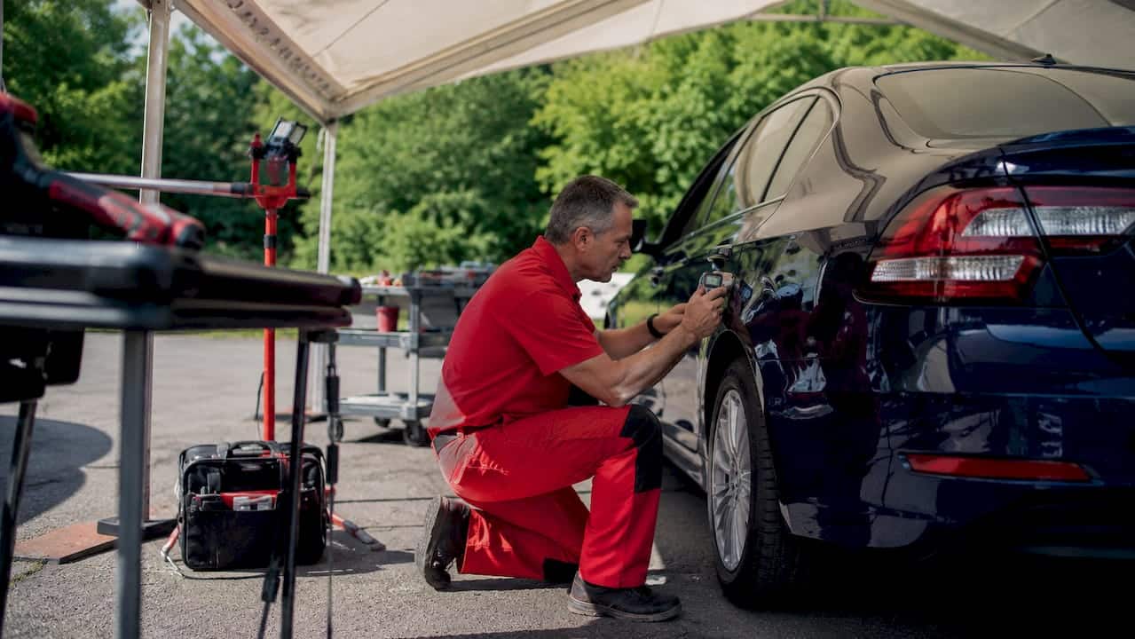 Technician inspecting damaged car in repair garage