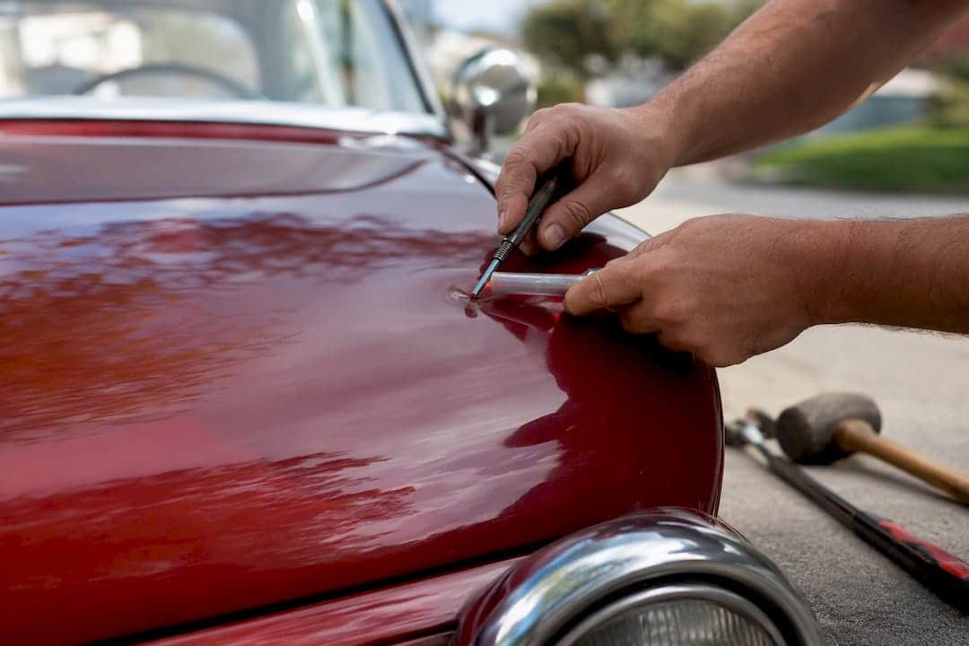 Technician hands repairing dent on vintage car door