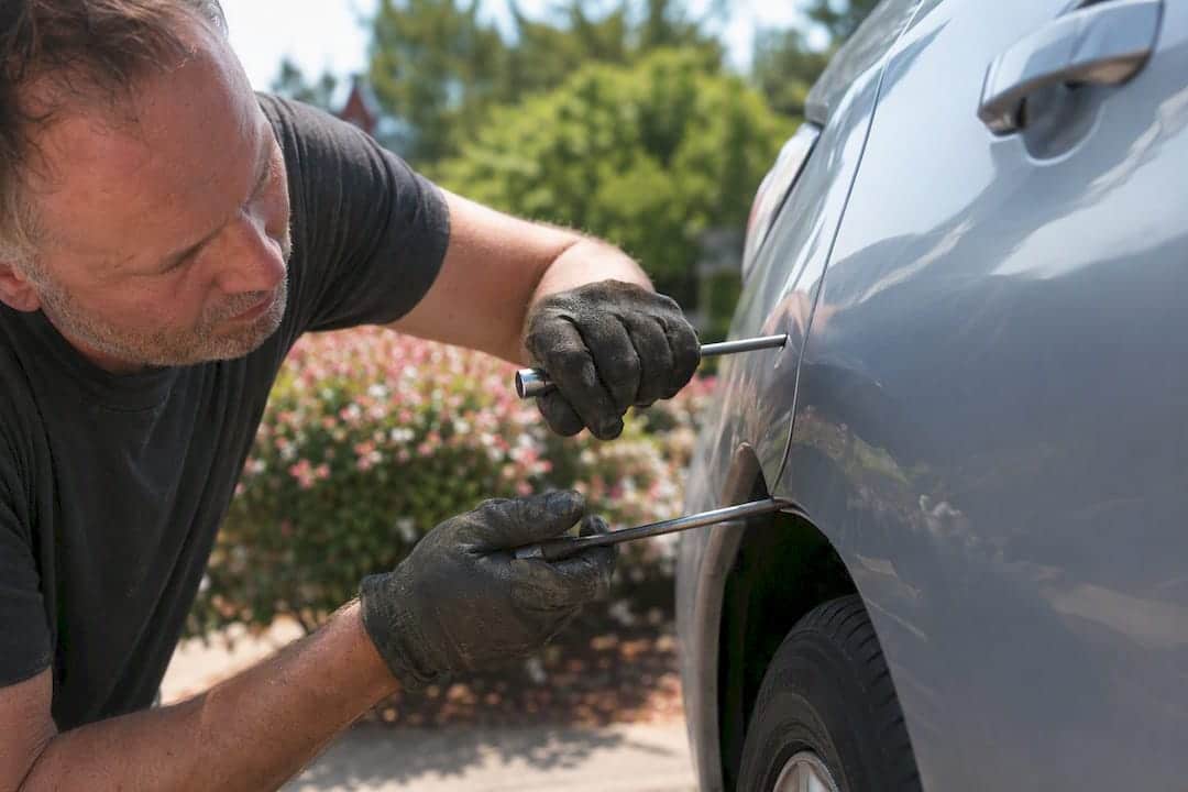 Hands repairing car dent with specialized tools