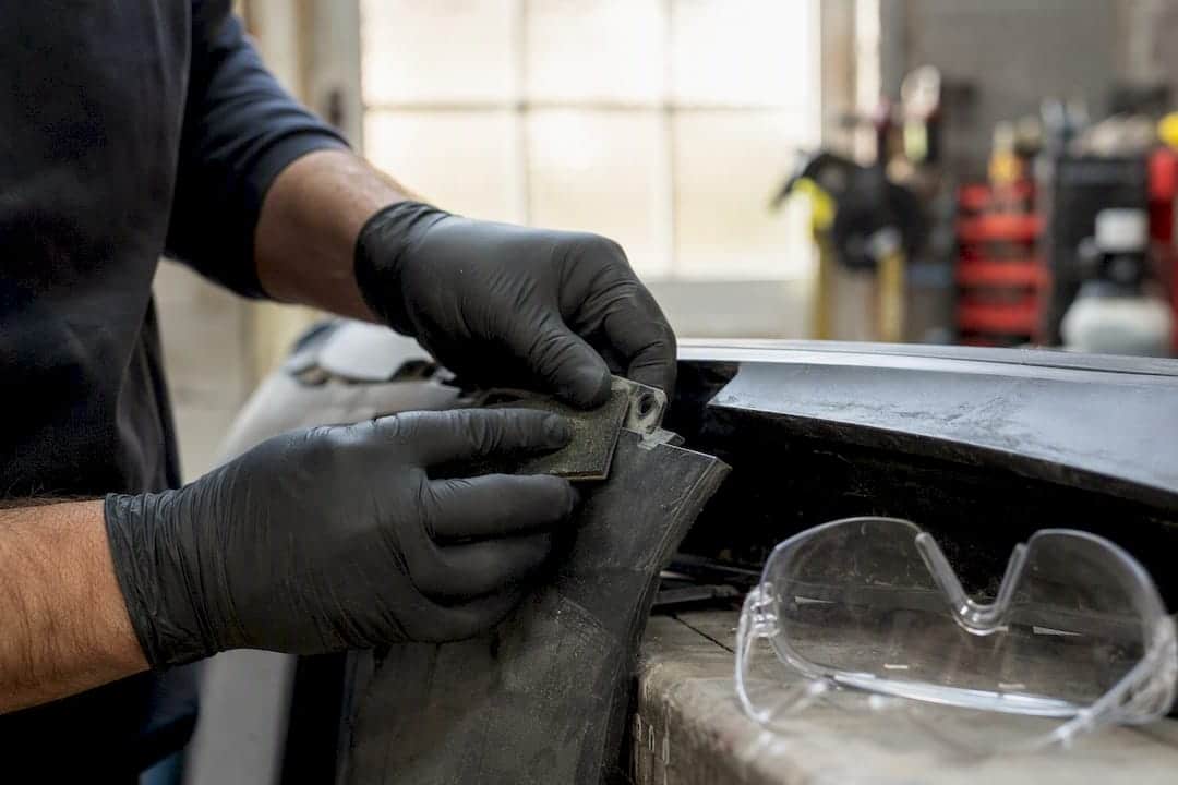 Bumper Tab Repair: Adhesive Rebuild vs Plastic Welding 1 Gloved Hands Sanding Tab With Eye Protection Nearby